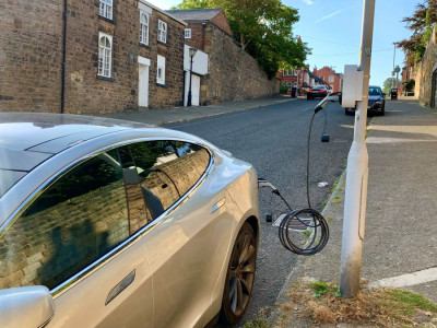 Silver car parked up at the side of the road and plugged into one of the electric vehicle charging points attached to the streetlight