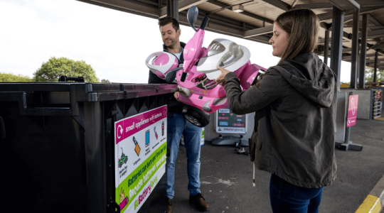 Two people recycling a child's toy at a Household Waste Recycling Centre