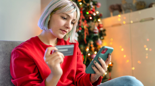 Photo of a lady holding a phone and bank card while sitting in front of a Christmas tree