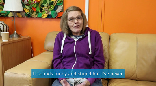 Lady in a purple hoodie sat on a sofa talking to camera