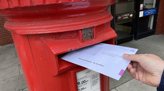 Photo of an envelope being posted into a post box.