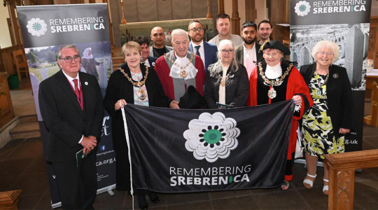 Photograph of the Mayor and Mayoress of Wirral, along with other civic leaders from across the city region, holding a Remembering Srebrenica flag.