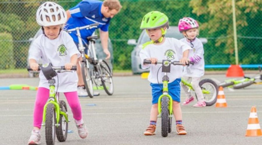 Three young children riding balance bikes around mini traffic cones.