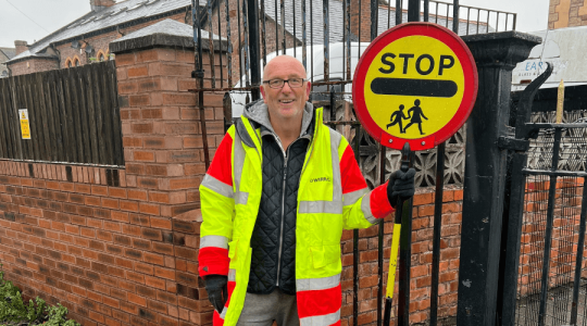 Photo of a person in a high vis jacket with the 'stop, children crossing' sign often referred to as a lollipop sign