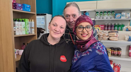 Three people smile for the camera inside of a food distribution point