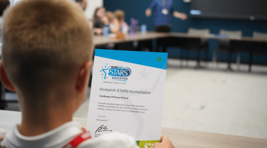 Back of a child's head as they look at a Modeshift certificate awarded to Castleway Primary School