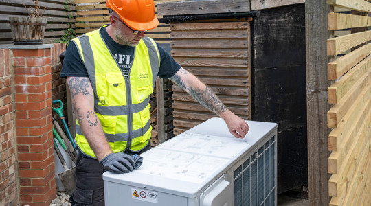 Stock image of a workman in high vis installing a heat pump in a garden