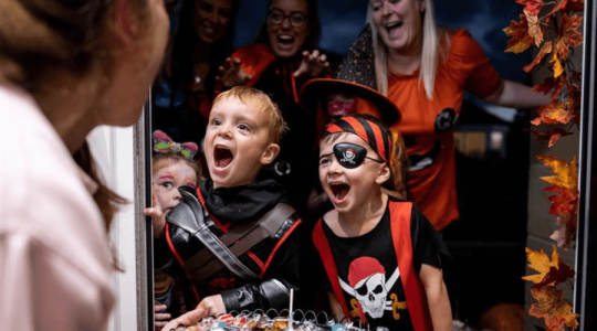 Some young children with their parents excited as they trick-or-treat at a person front door