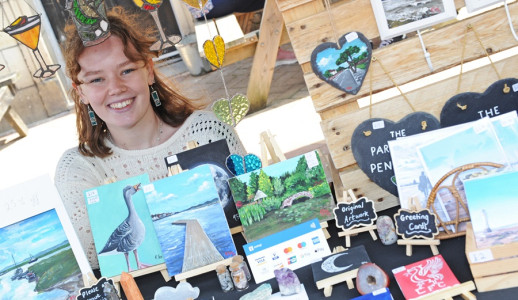 A young trader sat at their stall surrounded by the artwork they are selling