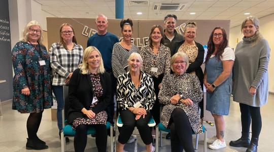 A group of 12 people smiling, some standing some sitting down