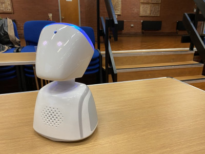 A white robot in the shape of a head and a torso sits on a wooden table