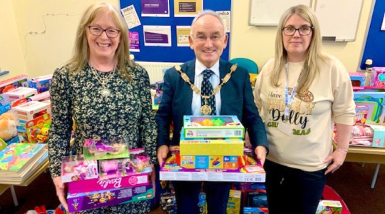Photo of the the Deputy Mayor and Mayoress holding a stack of gifts and a staff member from Wirral Council