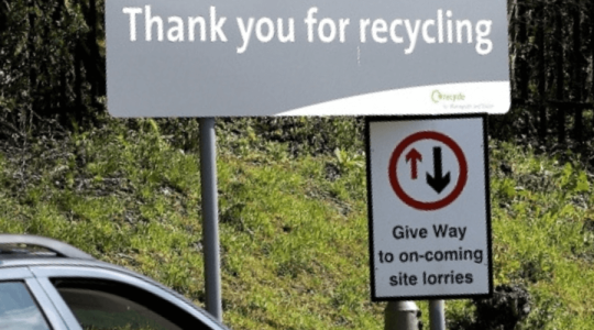 Close up where you can see part of a car pulling up at a tip and a sign that says 'thank you for recycling'