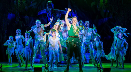 Photo of a triumphant Peter Pan on stage surrounded by the cast