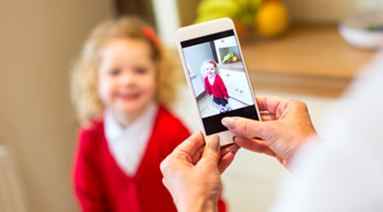 Little girl aged around 4 years old poses for a photograph from her mother in her new school uniform. 