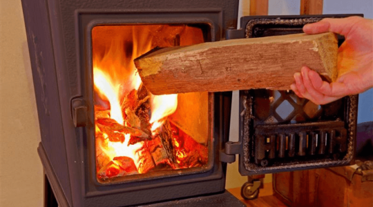 A close up of a hand placing a log into a log burner