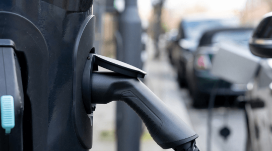 Close up of an eletric vehicle charging point plugged in and attached to a car that's on the street