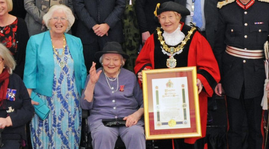 Photograph of Dame Patricia Routledge with the Mayor holding the freedom scroll and Mayoress