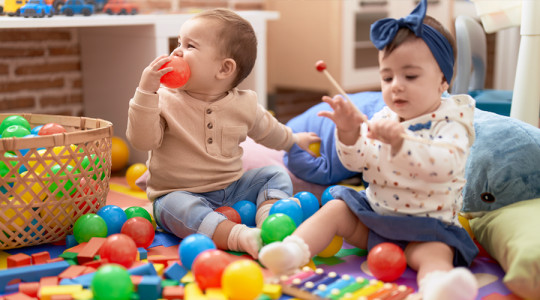 Two toddlers playing with balls and xylophone sitting on floor at nursery