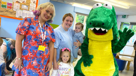 picture of two women and a child smiling to camera next to a person dressed in a dinosaur costume