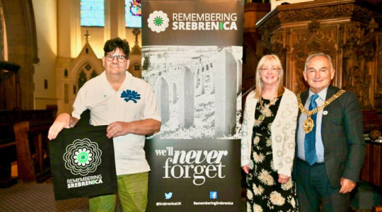 Photo of the Mayor and Mayoress and a representative of Srebrenica UK in front of a pull up banner which says Remembering Srebrenica