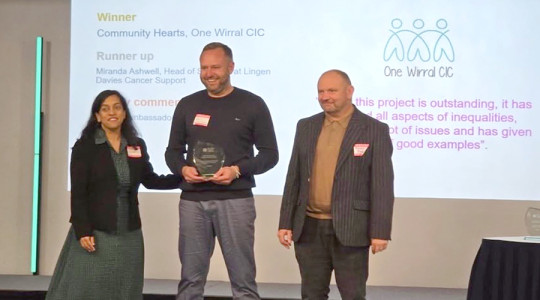 three people smile as they receive an award in front of a screen
