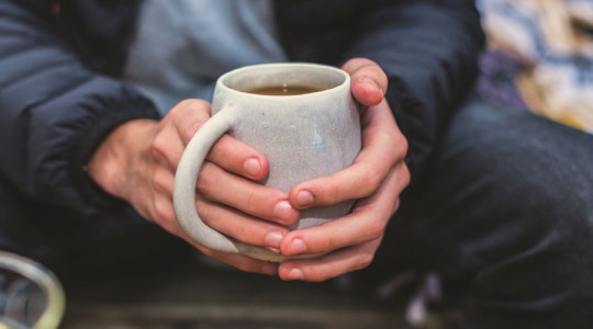 A pair of hands holding a white mug filled with tea.