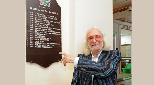 Photo of Charlie pointing to his name on a list of Freeman of Wirral on a wall plaque