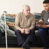 Young man and older man sitting on sofa looking at looking at ipad discussing services available in Wirral's social care