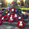 Multiple wreaths laid at the foot of stone cross in Thornton Hough with sun shining through trees