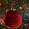 Close up of a red sparkly Christmas bauble hanging on a tree