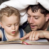 Dad reading book to son under bed covers