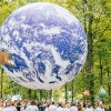 Photo of Gaia hovering above a crowd in a forest setting