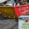 A sign saying 'Love where you live' with a full skip behind it