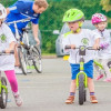 Three young children riding balance bikes around mini traffic cones.