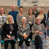 A group of 12 people smiling, some standing some sitting down