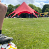 Close up of youth foot balancing on football with the Fostering big red tent in distance 