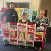 Three people holding up a handmade quilt. They are all smiling.