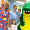 picture of two women and a child smiling to camera next to a person dressed in a dinosaur costume