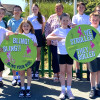 Children and adults from Greenleas school holding green signs promoting walking, cycling, and scooting to school, outside a residential area