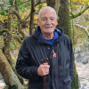 Senior man with holding walking stick, smiling at camera, next to the river on sunny autumn day