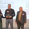 three people smile as they receive an award in front of a screen