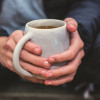 A pair of hands holding a white mug filled with tea.