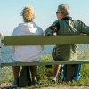 Man and woman witting on a bench by a beach with their back to us