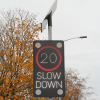 Close up of one of the traffic signs installed - it is a black sign with LED lights that will shine if cars are going too quickly to illuminate the 20mph speed limit and the words 'slow down' and a solar panel at the top which powers the sign