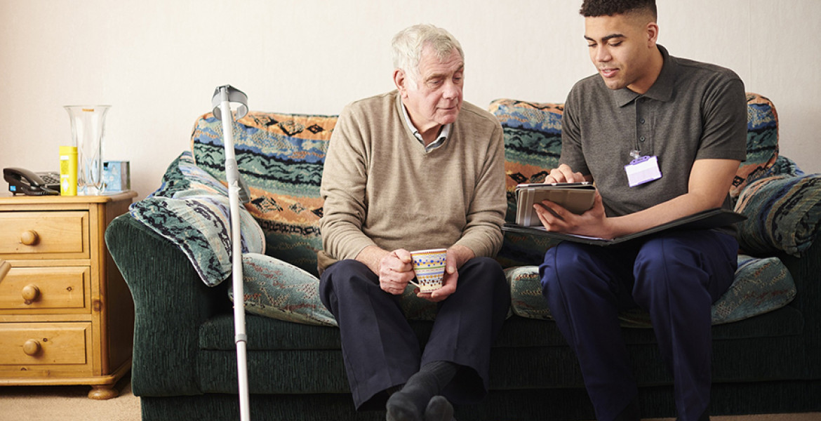 Young man and older man sitting on sofa looking at looking at ipad discussing services available in Wirral's social care