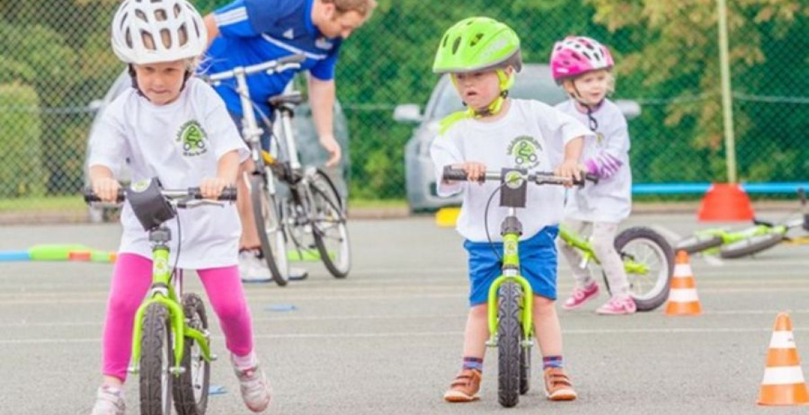 Three young children riding balance bikes around mini traffic cones.