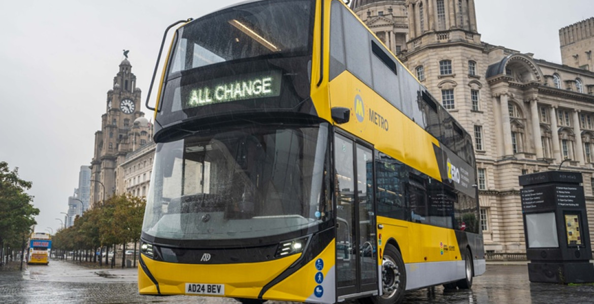 a new metro bus pictured in front of Liverpool's 3 graces, in bright yellow with "all change" where the number usually is
