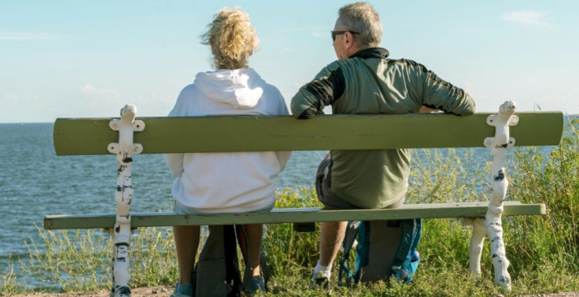 Man and woman witting on a bench by a beach with their back to us